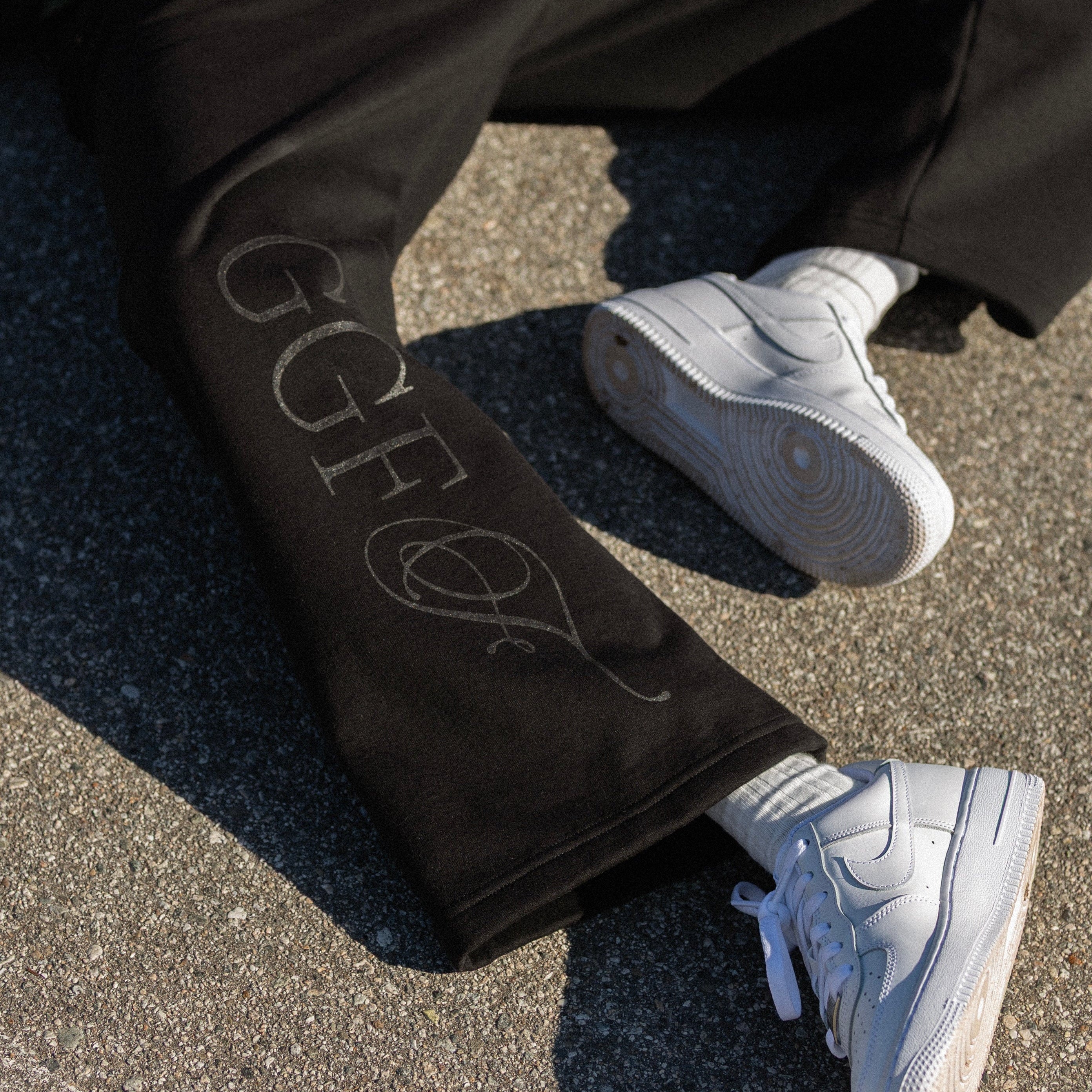 Person wearing black pants with 'GGFF' branding and white sneakers on a concrete surface.