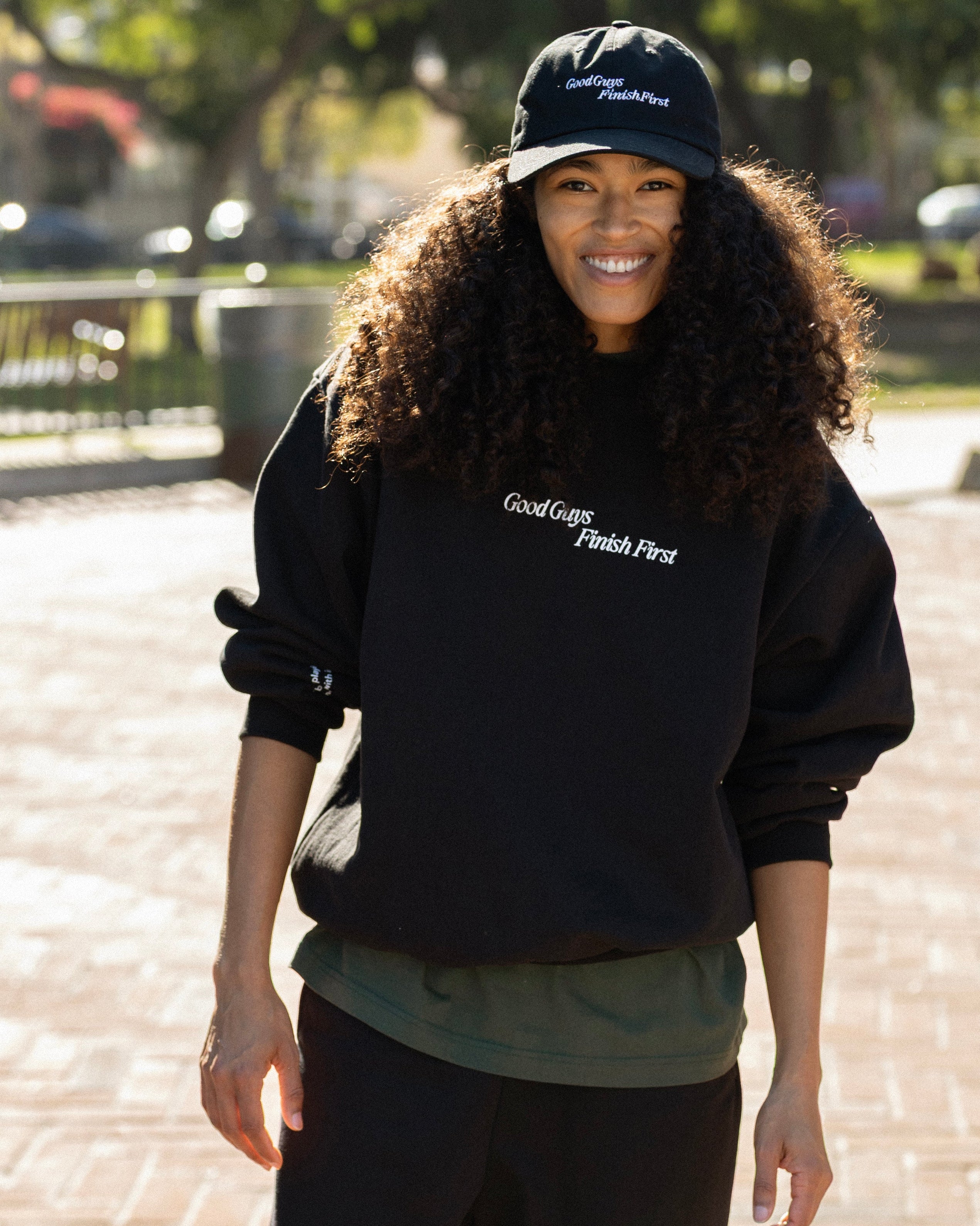 Person wearing a black sweatshirt and cap with text, standing outdoors.