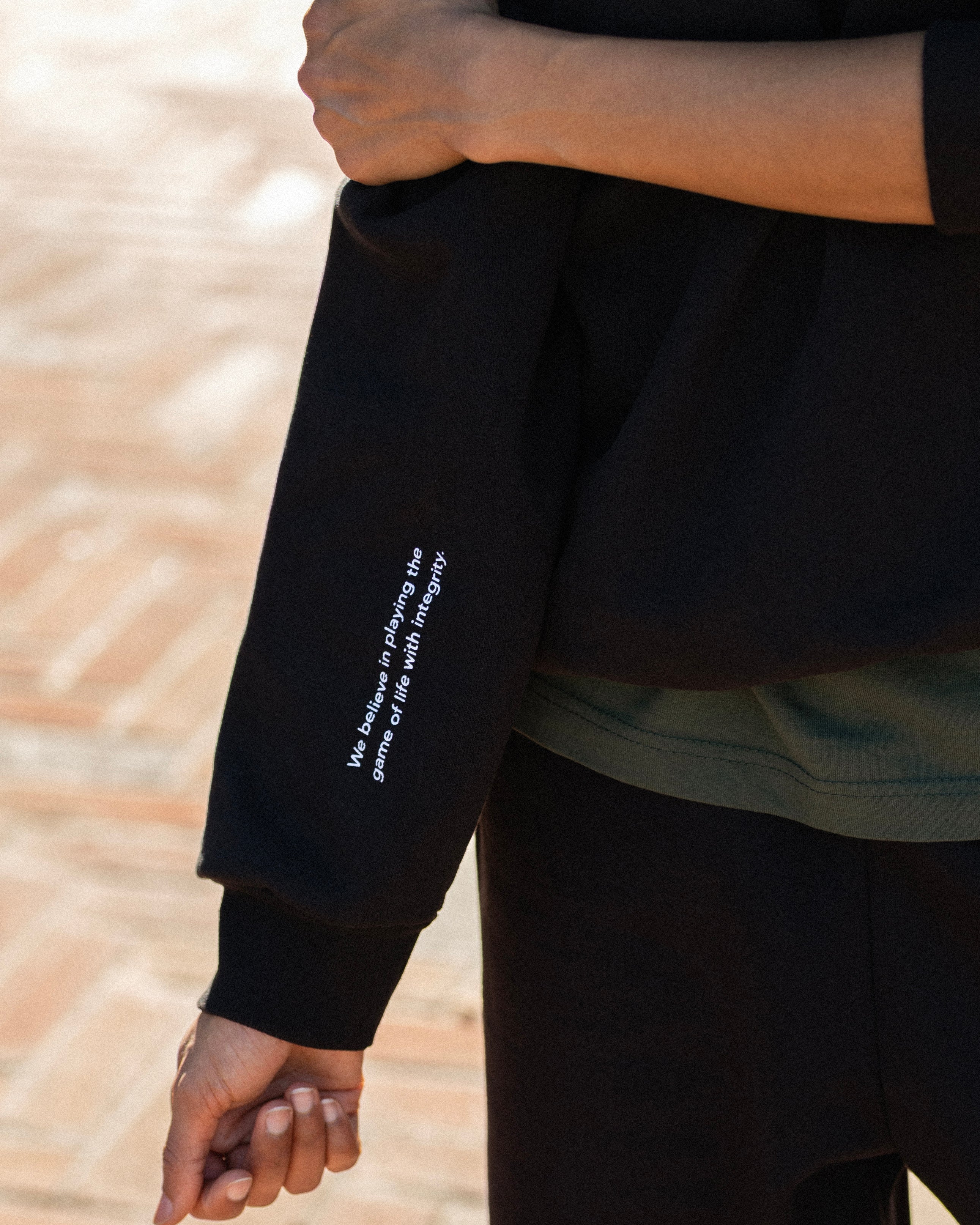 Person wearing a black sweatshirt with text on the sleeve, standing on a brick surface.