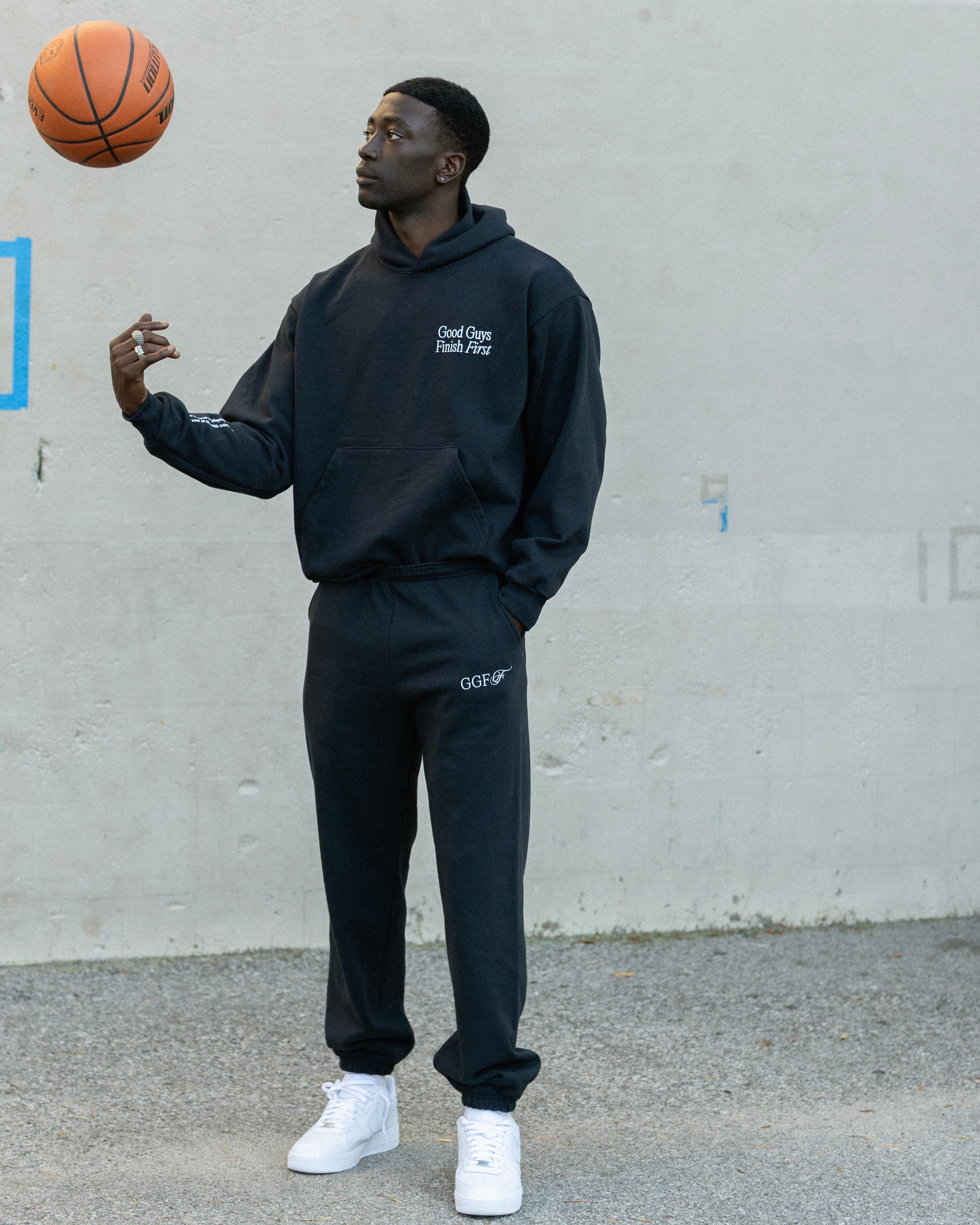 Person wearing a navy hoodie and pants holding a basketball against a gray wall.