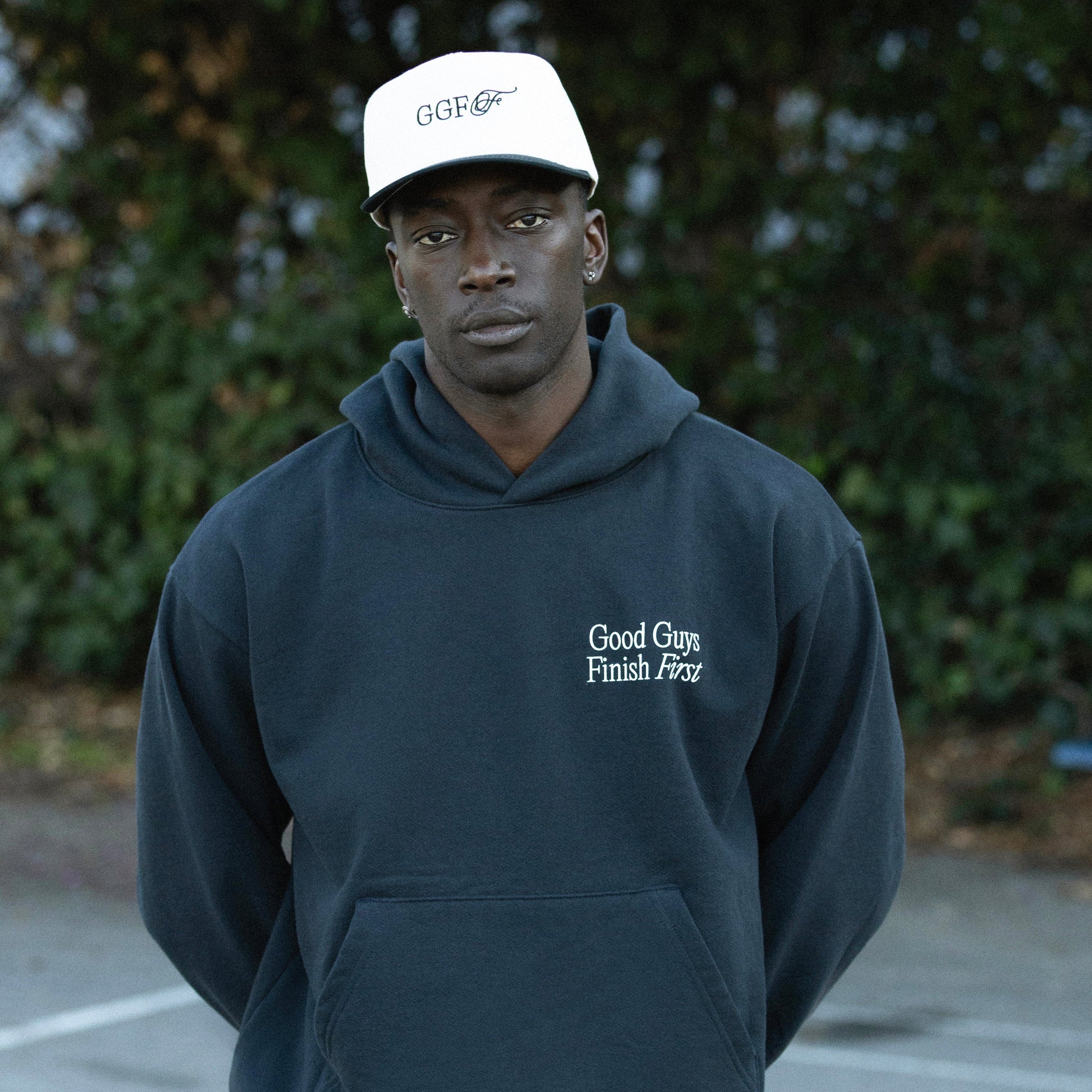 Person wearing a navy hoodie and pants with 'Good Guys Finish First' branding, standing outdoors.
