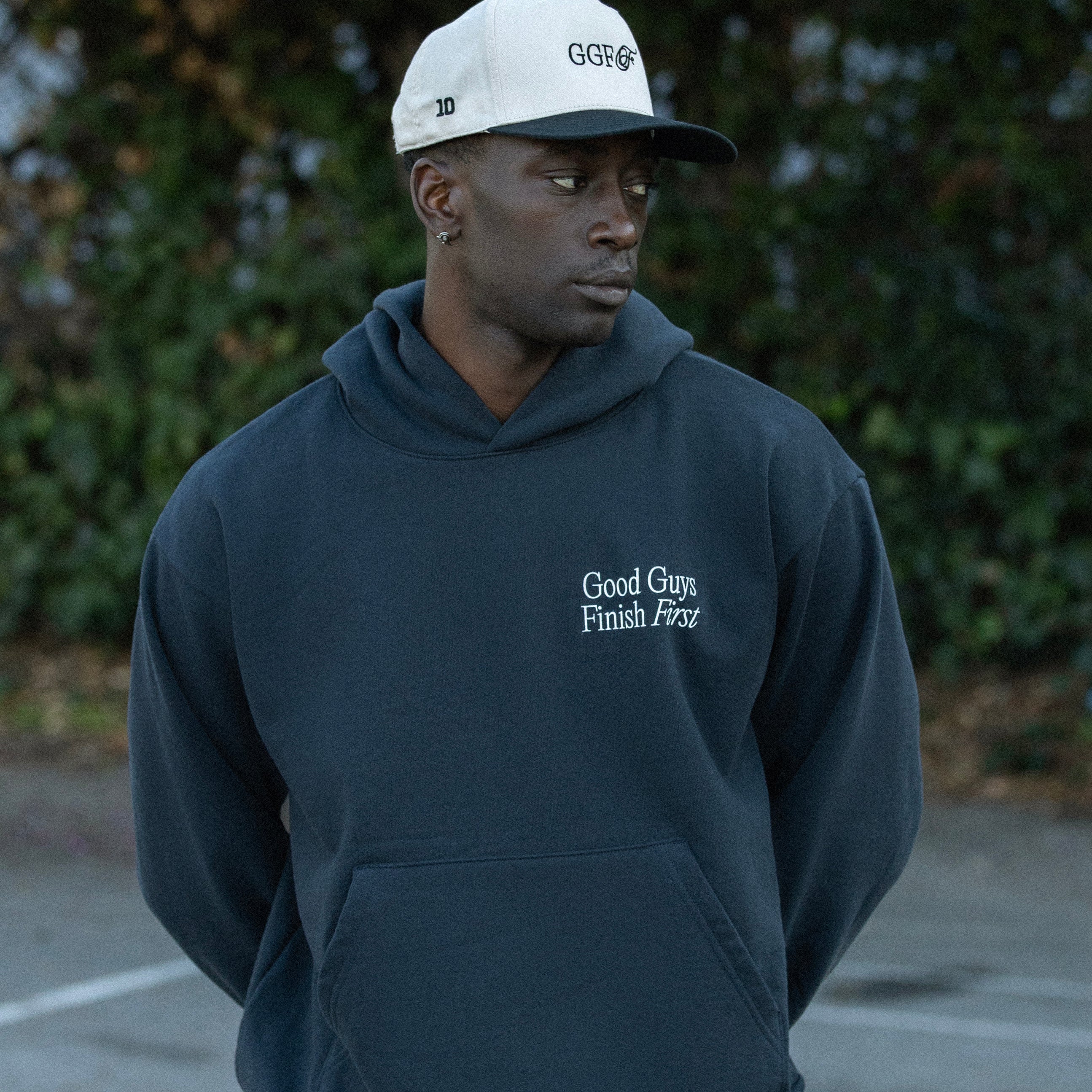 Person wearing a navy hoodie and white cap with text, standing outdoors.