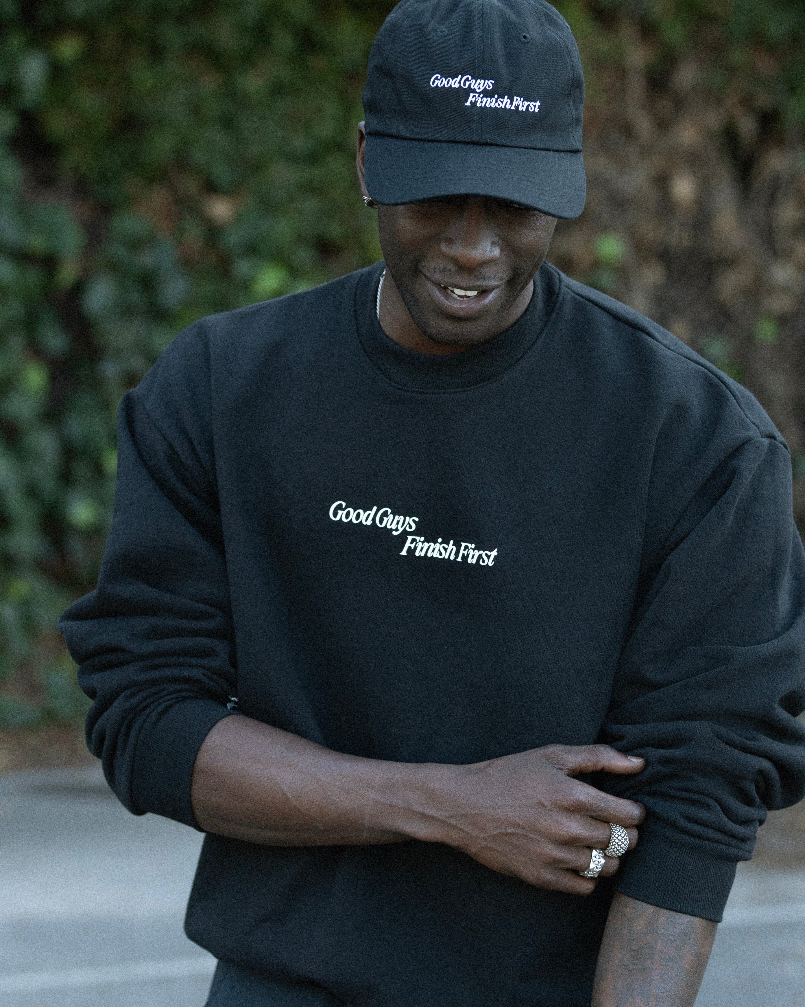 Person wearing a black sweatshirt and cap with 'Good Guys Finish First' text, standing outdoors.